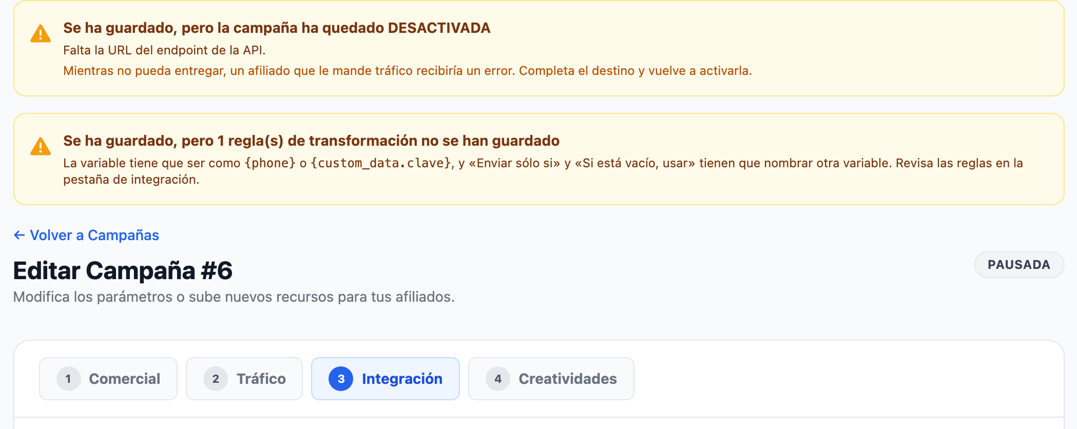 Ficha de una campaña tras guardar: aviso ámbar «Se ha guardado, pero la campaña ha quedado DESACTIVADA» con el motivo «Falta la URL del endpoint de la API.», otro aviso «Se ha guardado, pero 1 regla(s) de transformación no se han guardado» y, debajo, el título con la insignia «Pausada» y las pestañas con «Integración» abierta.
